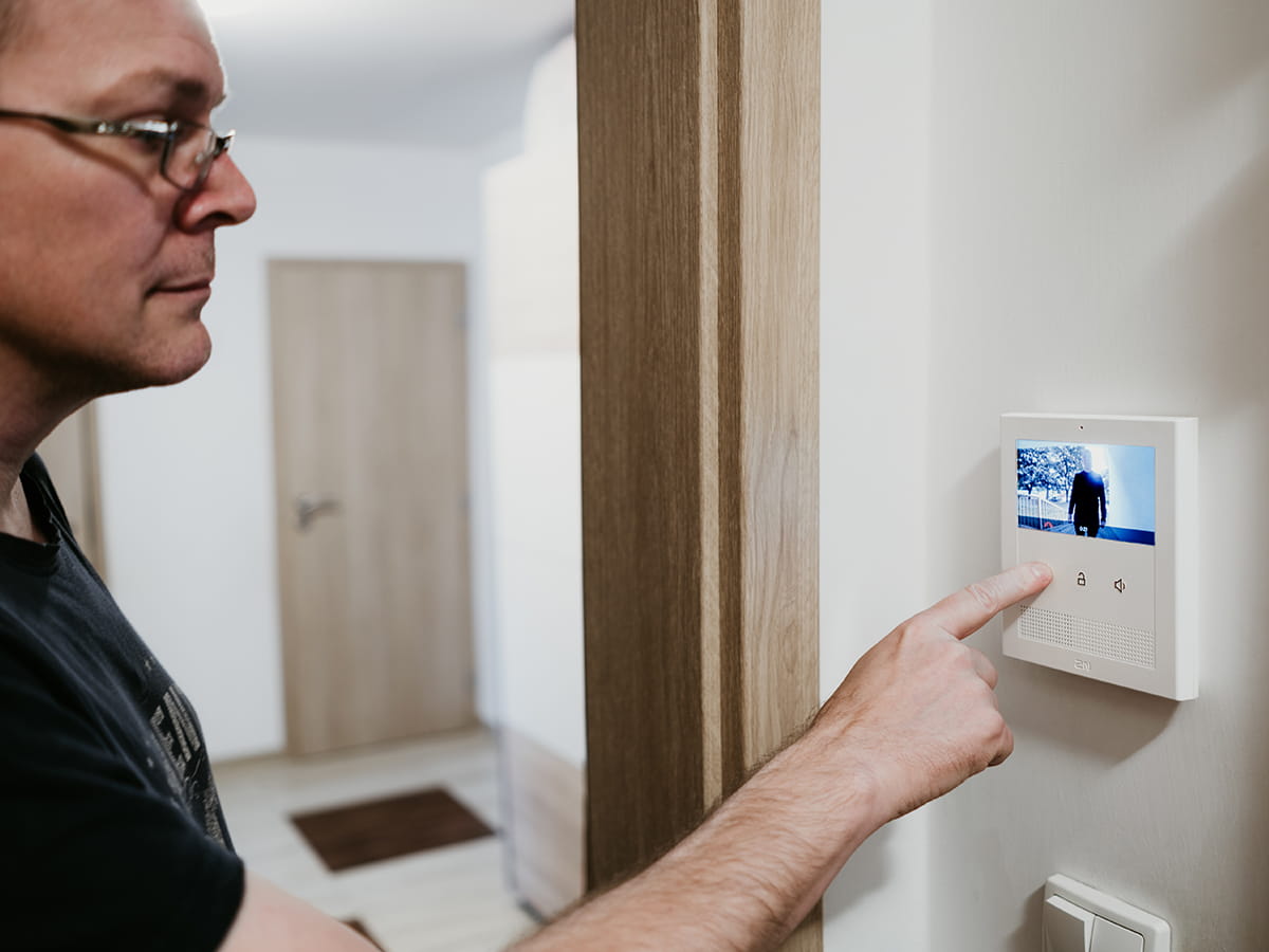 Personne interagissant avec un écran de vidéophone mural dans un couloir moderne.