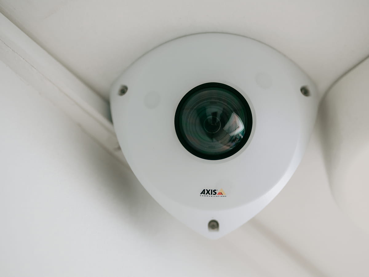 Gros plan sur une caméra de sécurité triangulaire blanche montée au plafond pour la surveillance intérieure.
