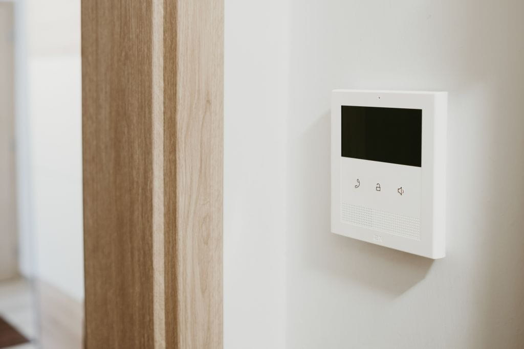 Dispositif de vidéophone mural avec un écran noir et trois boutons dans un couloir moderne.