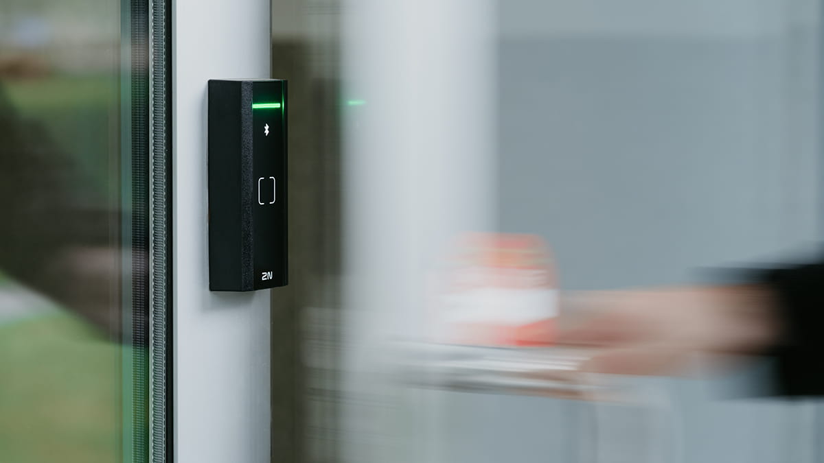 Personne tenant une carte d'accès près d'un lecteur RFID noir avec une lumière verte sur une porte en verre.
