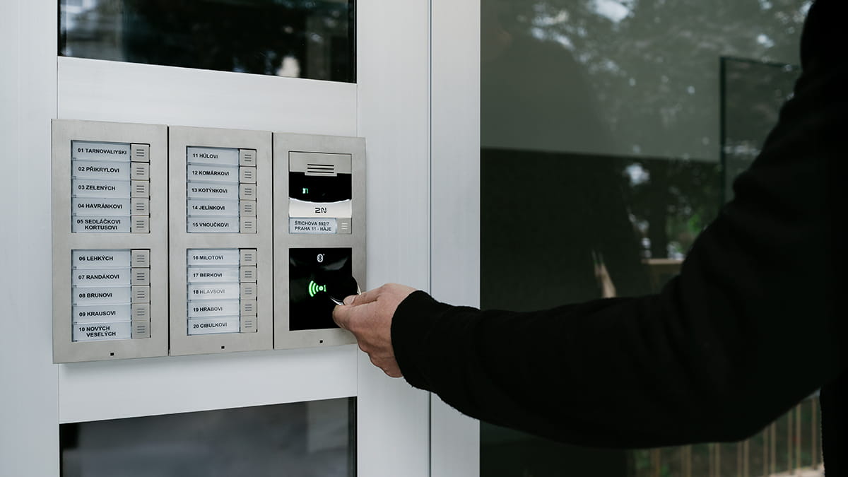 Quelqu'un utilise un badge RFID sur un panneau d'interphone extérieur à plusieurs boutons pour entrer en toute sécurité.