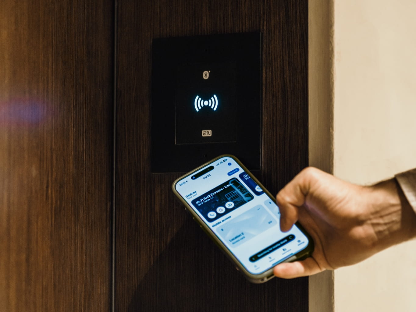 Une main tient un smartphone près d'un lecteur de carte pour une ouverture de porte sans contact.