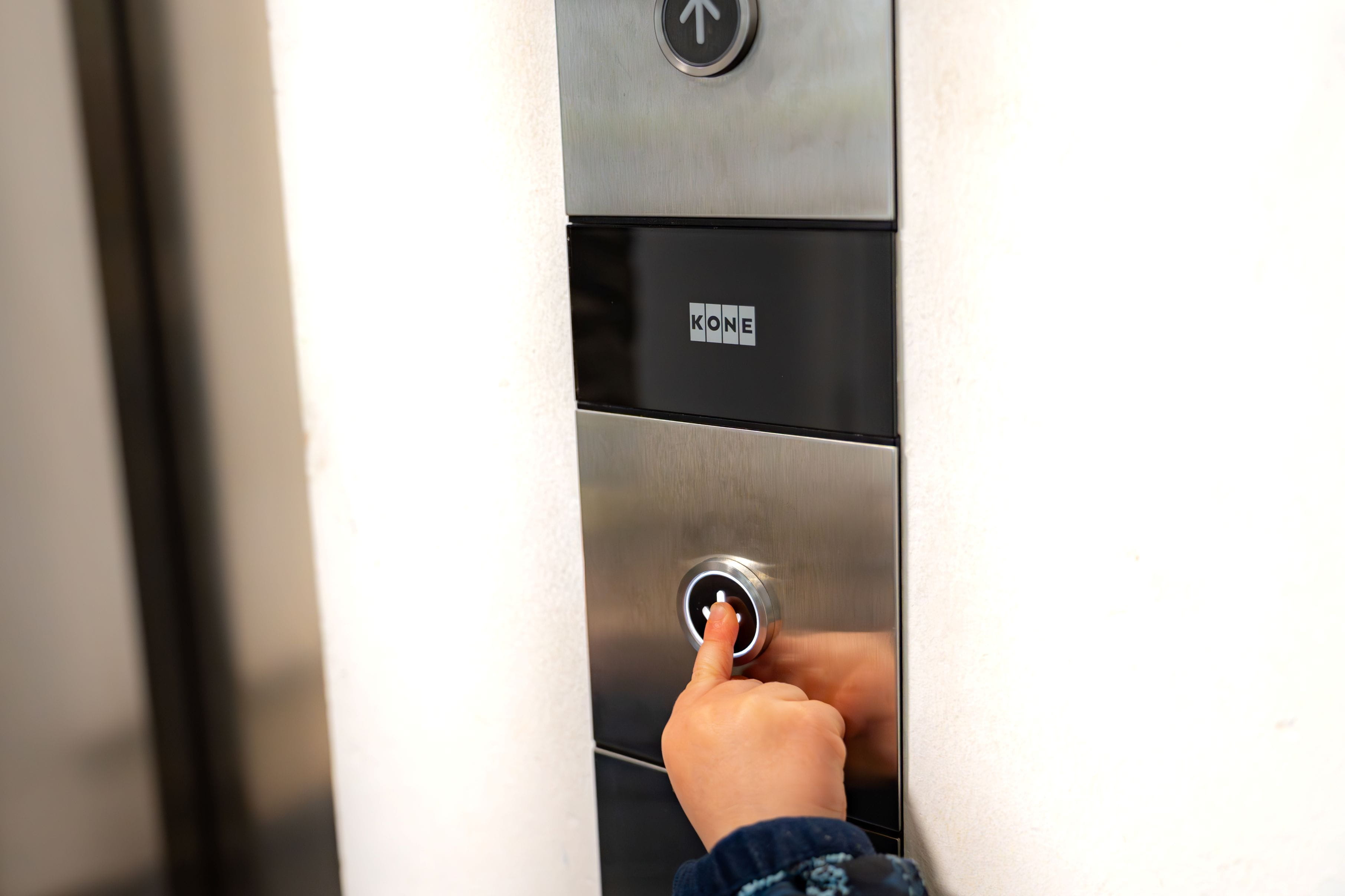 Close-up van een hand die op een liftoproepknop drukt op een metalen bedieningspaneel.