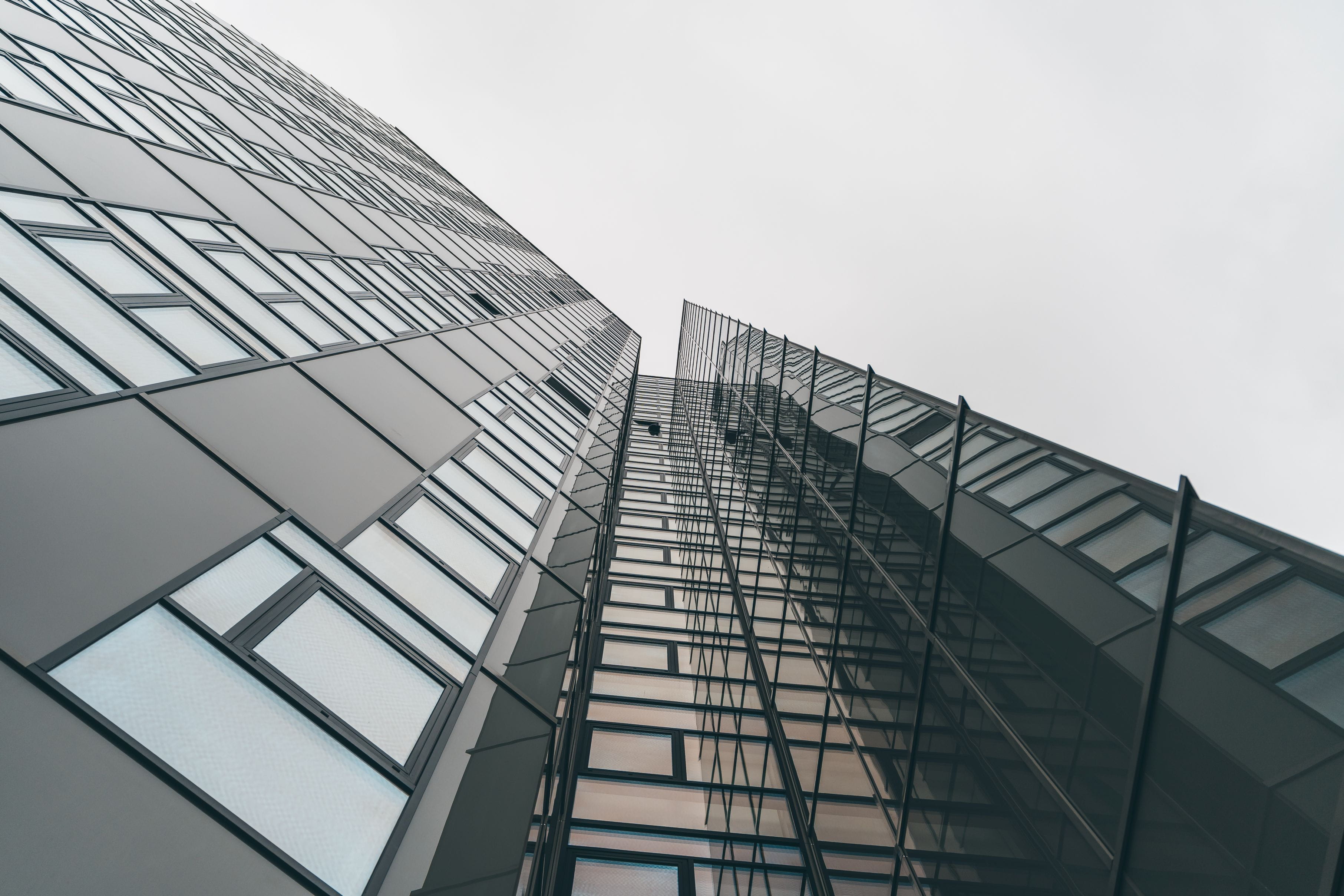 Opwaartse kijk op een hoog modern glazen gebouw met reflecterende panelen tegen een bewolkte lucht.