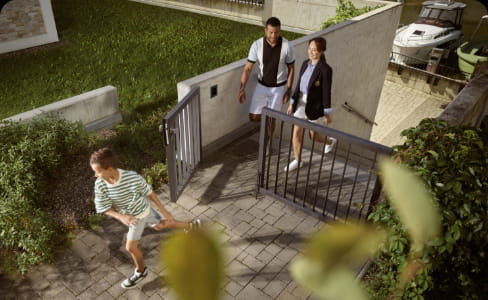 Child running through a residential gate while adults follow, outdoor pathway by the water
