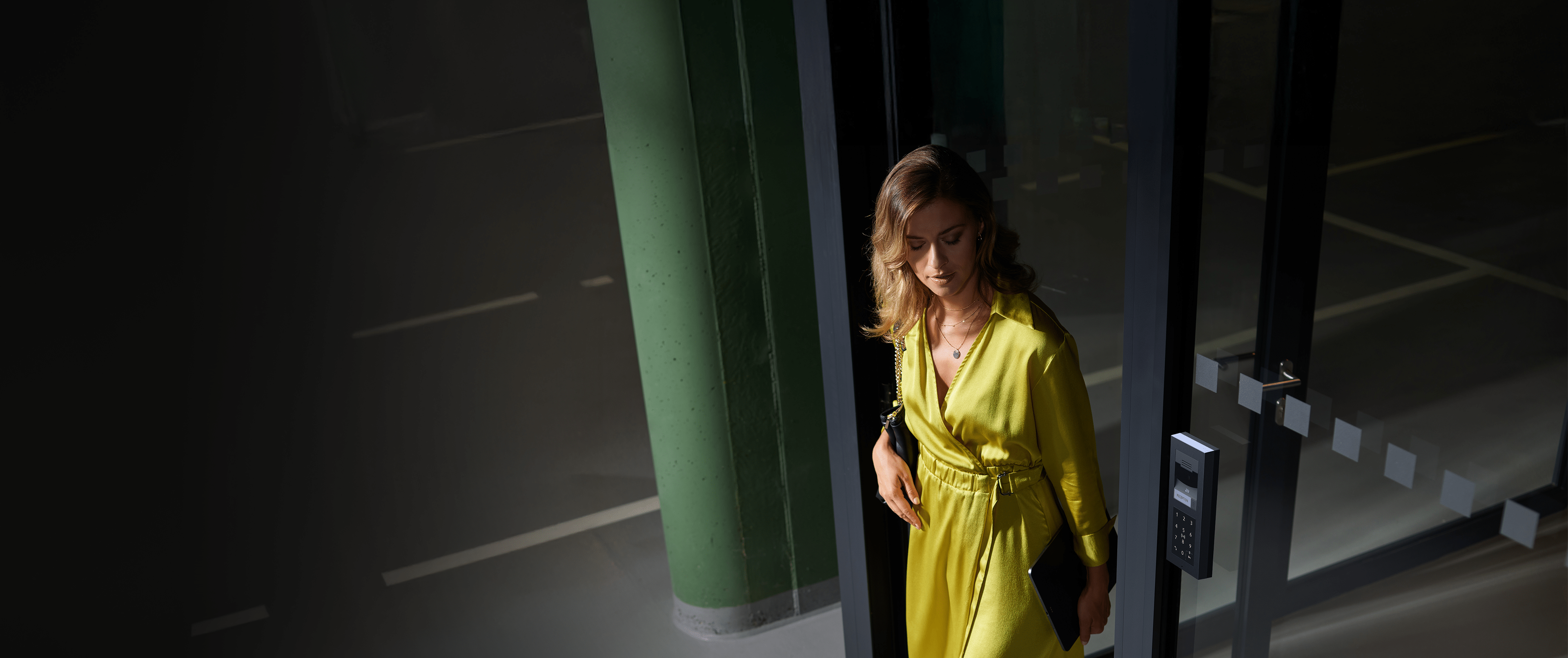 Woman entering through a glass door using a 2N intercom door reader